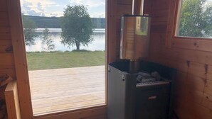 A cabin with a wood-burning stove, a small stool, and a view of a lake.