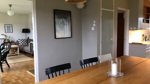 A dining area with a wooden table, black chairs, a clear glass candle holder, a framed picture on the wall, and a doorway leading to another room.