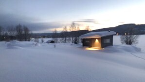 A snow-covered landscape with a small cabin illuminated by warm light.