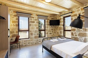 A bedroom with stone walls, a bed, a chair, a TV, and a window. - New Luxurious Villa With Stunning Pool,views &bbq! (Rethymno)