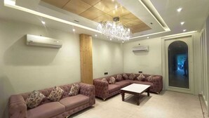 A modern living room with two sofas, a coffee table, a chandelier, and a door leading to another room. - Townhouse Rambagh Amritsar (Amritsar)