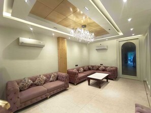 A modern living room with two sofas, a coffee table, a chandelier, and a door leading to another room. - Townhouse Rambagh Amritsar (Amritsar)