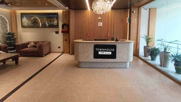 A reception desk labeled 'TOWNHOUSE' with a chandelier, wooden paneling, a sofa, and potted plants. - Townhouse Rambagh Amritsar (Amritsar)