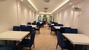 A restaurant with tables and chairs arranged in rows, a ceiling fan, and a view of a garden through arched windows. - Townhouse Rambagh Amritsar (Amritsar)