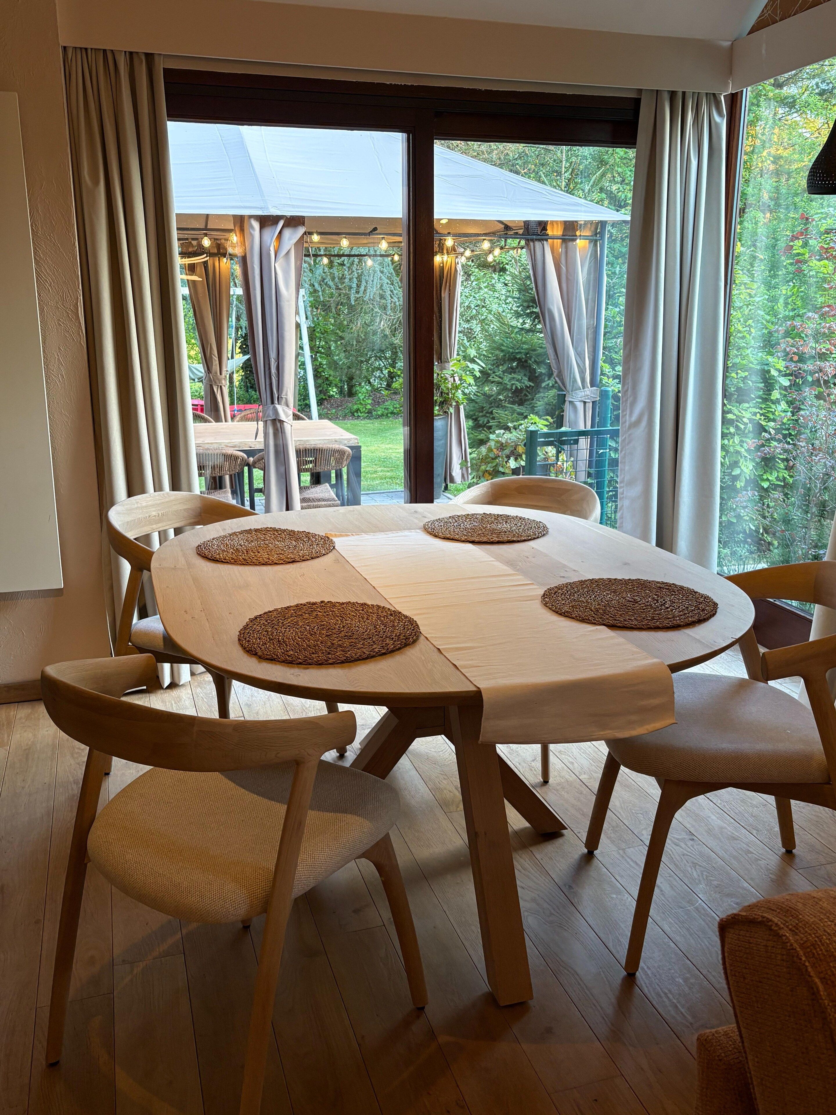 Un coin repas avec une table ronde, six chaises et des sets de table en fibres tressées.