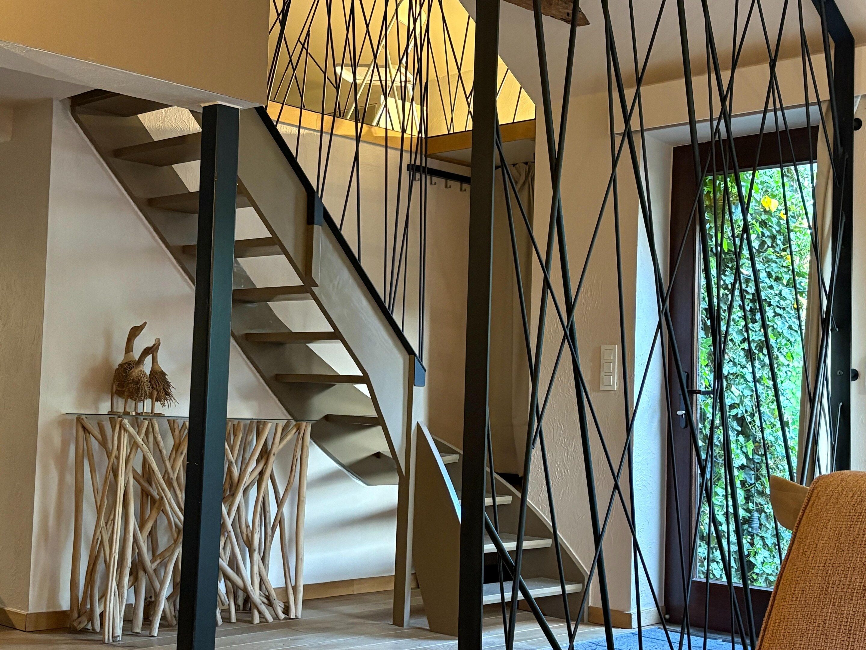 A staircase with a modern design, a wooden side table with a decorative item, and a view of greenery through a door.