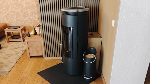 A modern living room with a black cylindrical heater, a black trash bin, a wooden side table, and a black mat on the floor. - Plein Sud La Roche en Ardenne (La Roche-en-Ardenne)