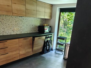 Eine Küche mit Holzausstattung, einer Arbeitsfläche, einer Waschmaschine und Blick auf Grünflächen.