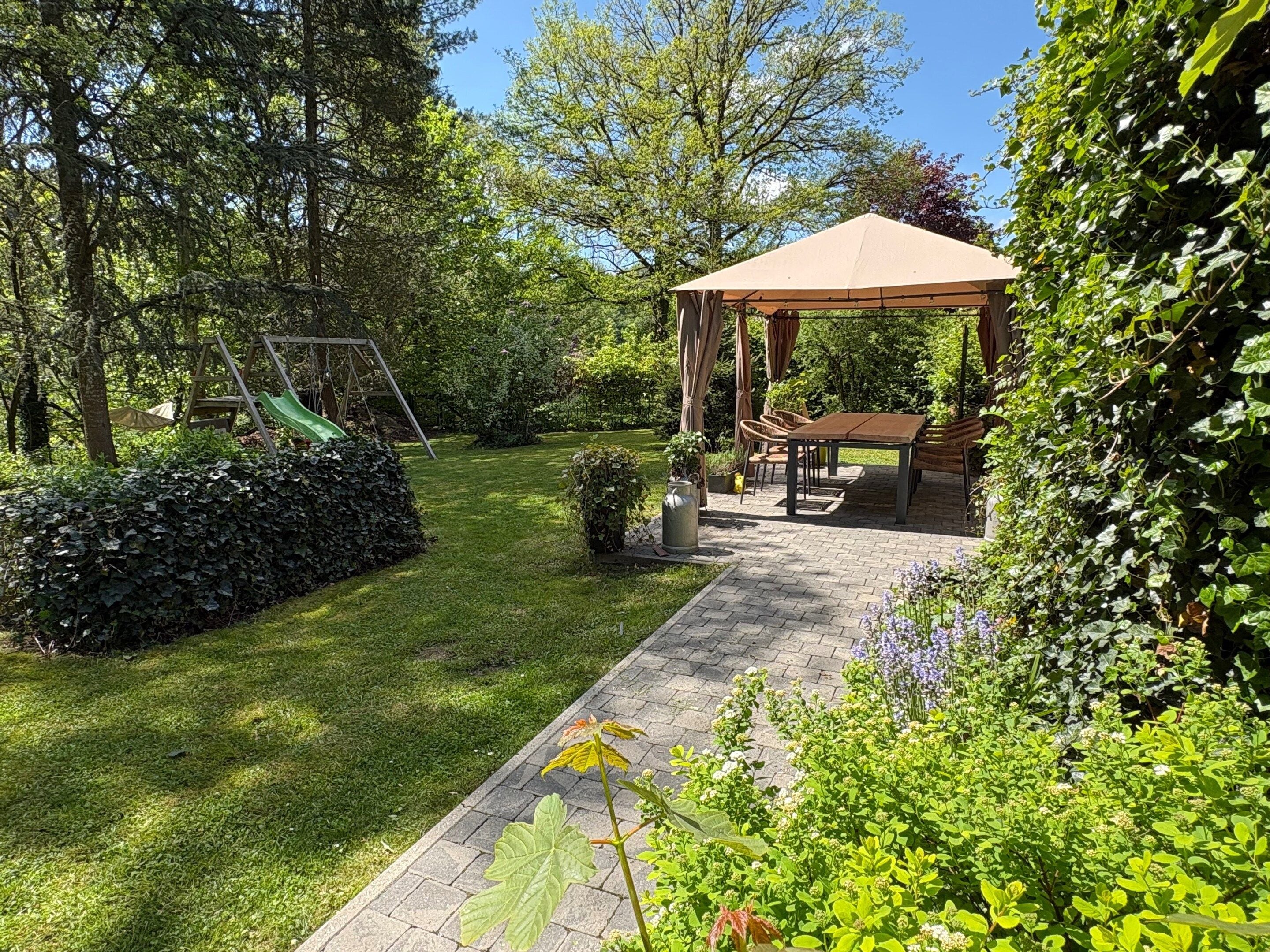 A garden with a gazebo, a swing set, and a paved patio area.
