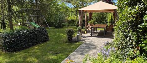 A garden with a gazebo, a swing set, and a paved patio area.