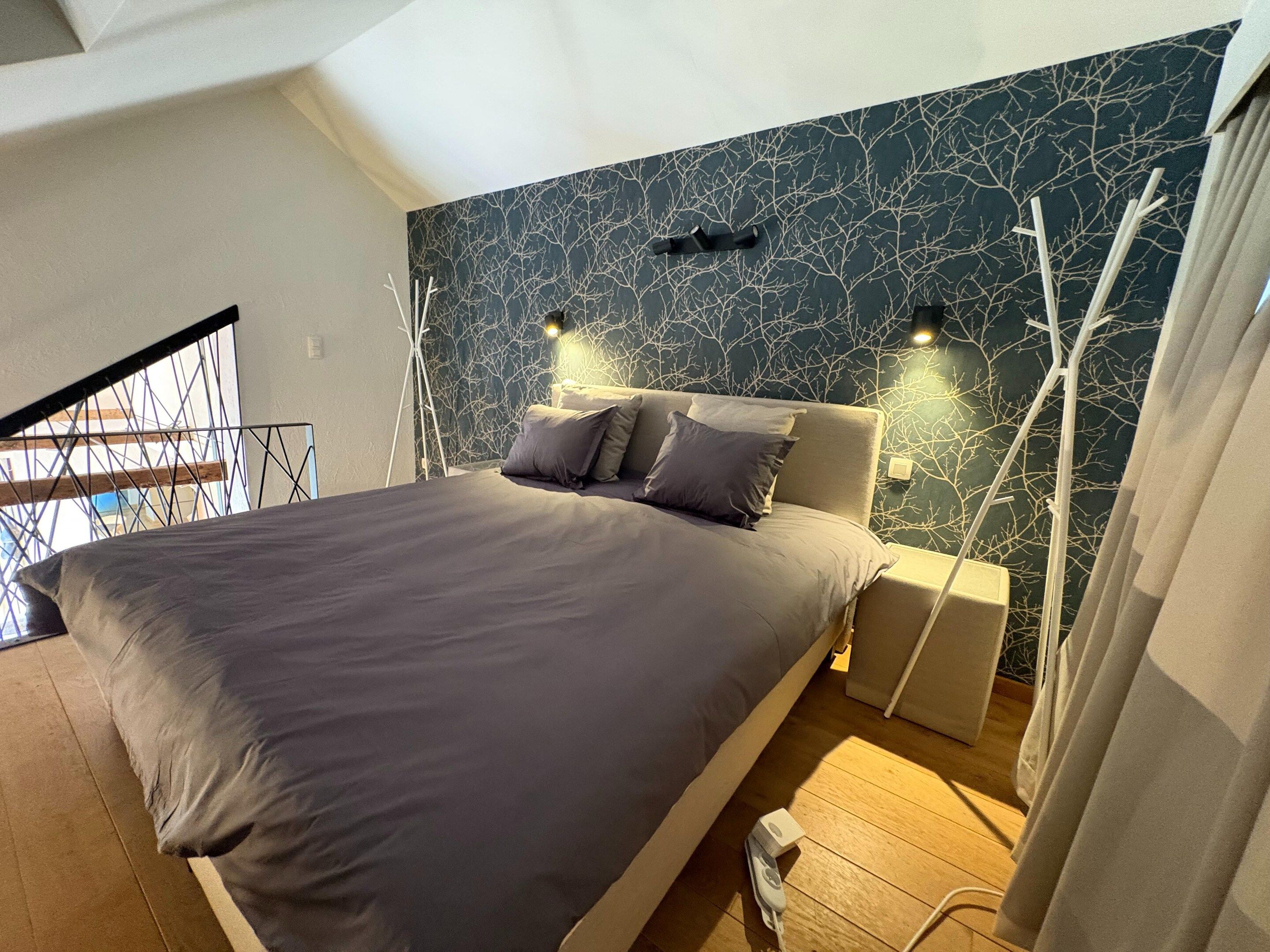 A modern bedroom with a large bed, a dark patterned wall, and a staircase.