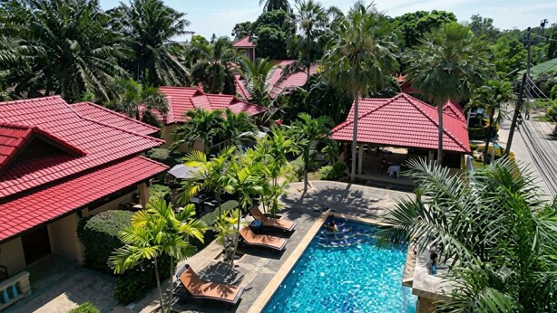 Un resort con piscina, edificios de techo rojo y palmeras.