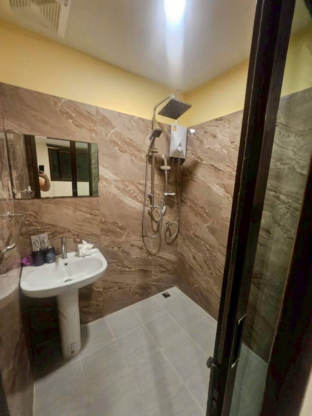 A bathroom with a marble wall, a sink, a shower, and a glass shower door.