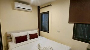 Una habitación de hotel con cama, aire acondicionado, ventana con persiana y una mesita.