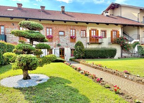 A two-story building with a brick facade, a tiled roof, and a well-maintained garden with hedges and flower beds.