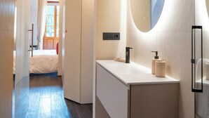 A modern bathroom with a white vanity, a large mirror, and a door leading to a bedroom. - Azalèe Apartment (San Maurizio Canavese)