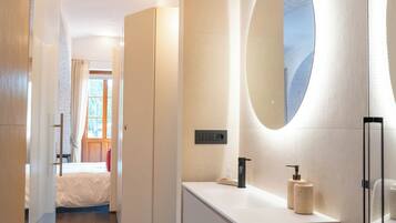 A modern bathroom with a white vanity, a large mirror, and a door leading to a bedroom.