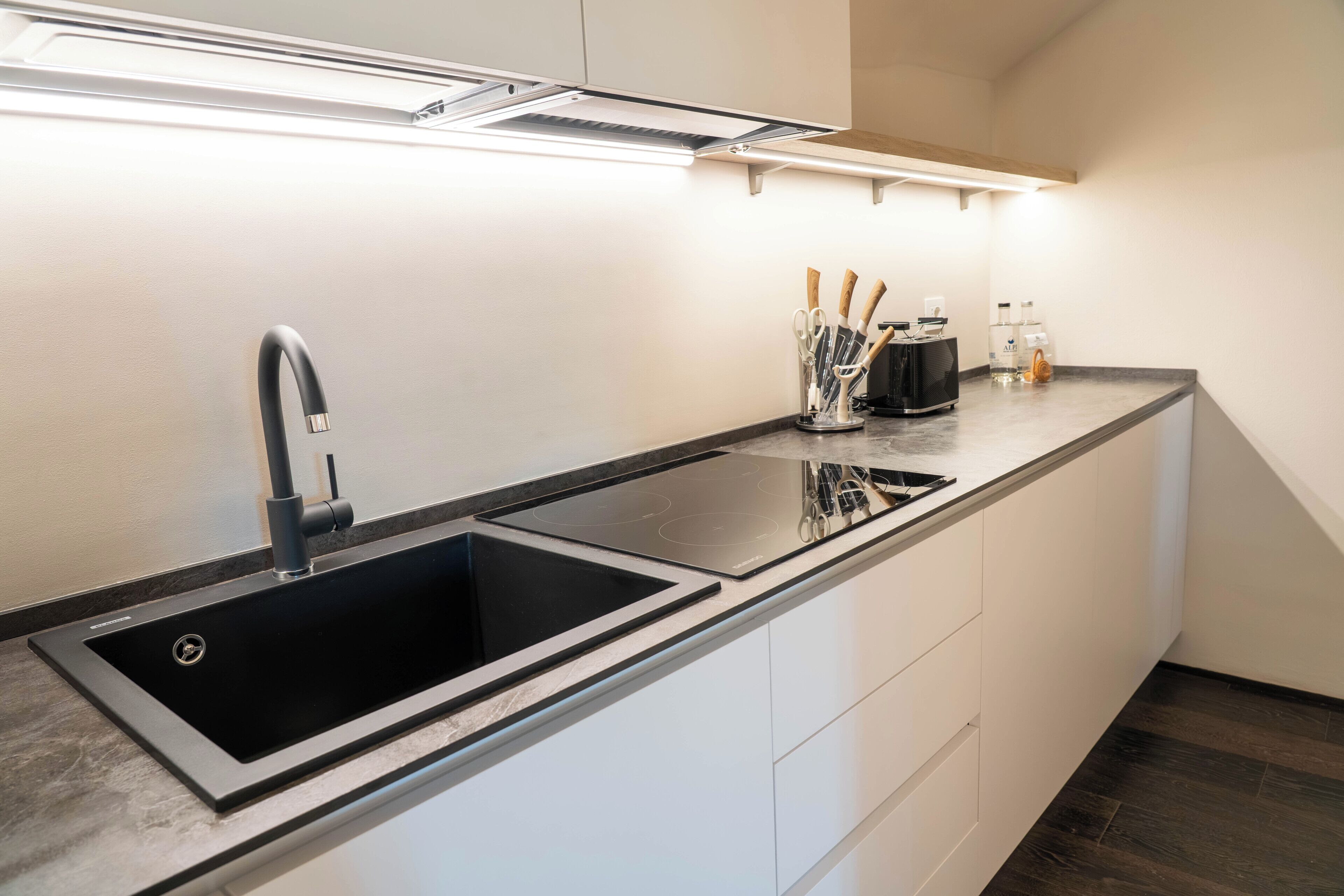 Een moderne keuken met een zwarte spoelbak, witte kasten en een aanrecht met keukengerei.