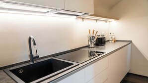 A modern kitchen with a black sink, white cabinets, and a countertop with utensils. - Azalèe Apartment (San Maurizio Canavese)
