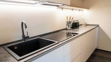 Een moderne keuken met een zwarte spoelbak, witte kasten en een aanrecht met keukengerei.