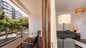 Un balcón con una mesa y sillas, un sofá, una lámpara y vistas a edificios y árboles.