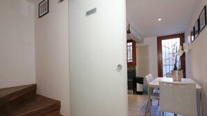 Eine Treppe führt zu einem Essbereich mit Tisch und Stühlen, einem Heizkörper und einem Fenster mit Jalousien.