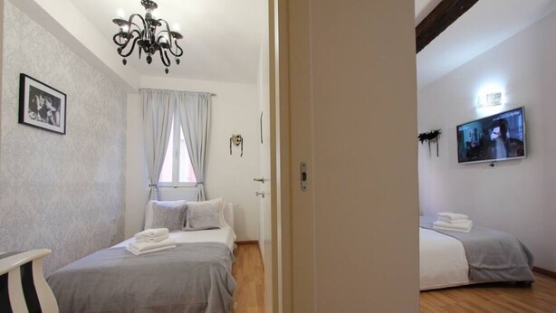 Ein Schlafzimmer mit Bett, einer Deckenleuchte, einem Fernseher und einem Fenster mit Vorhängen.