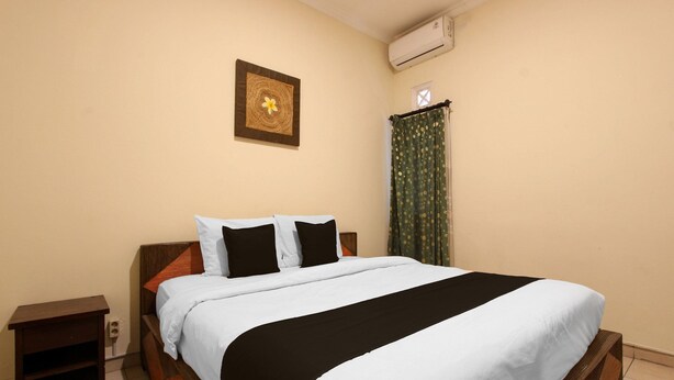 A neatly made bed with a white and black bedspread, a wooden headboard, a small wooden nightstand, a wall-mounted air conditioner, and a framed picture on the wall. - Spacious 2BR Villa Near Malioboro (Yogyakarta)