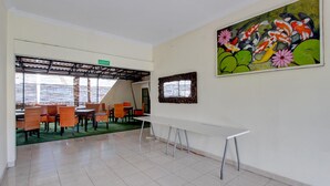 A spacious room with a long white table, orange chairs, a green carpet, and a large painting of koi fish and flowers on the wall. - Spacious 2BR Villa Near Malioboro (Yogyakarta)