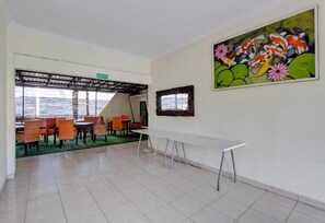 A spacious room with a long white table, orange chairs, a green carpet, and a large painting of koi fish and flowers on the wall. - Spacious 2BR Villa Near Malioboro (Yogyakarta)