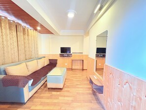 Een woonkamer met een bank, een salontafel en twee televisieschermen bevestigd aan houten wanden.