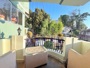 Un balcon doté d’une paroi en verre, d’une rambarde en métal et offrant une vue sur les arbres et les bâtiments.