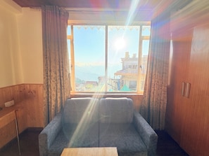A room with a sofa, a wooden table, and a window with a view of buildings and mountains. - Himayan Hotel Retreat near NCC Rd (Darjeeling)