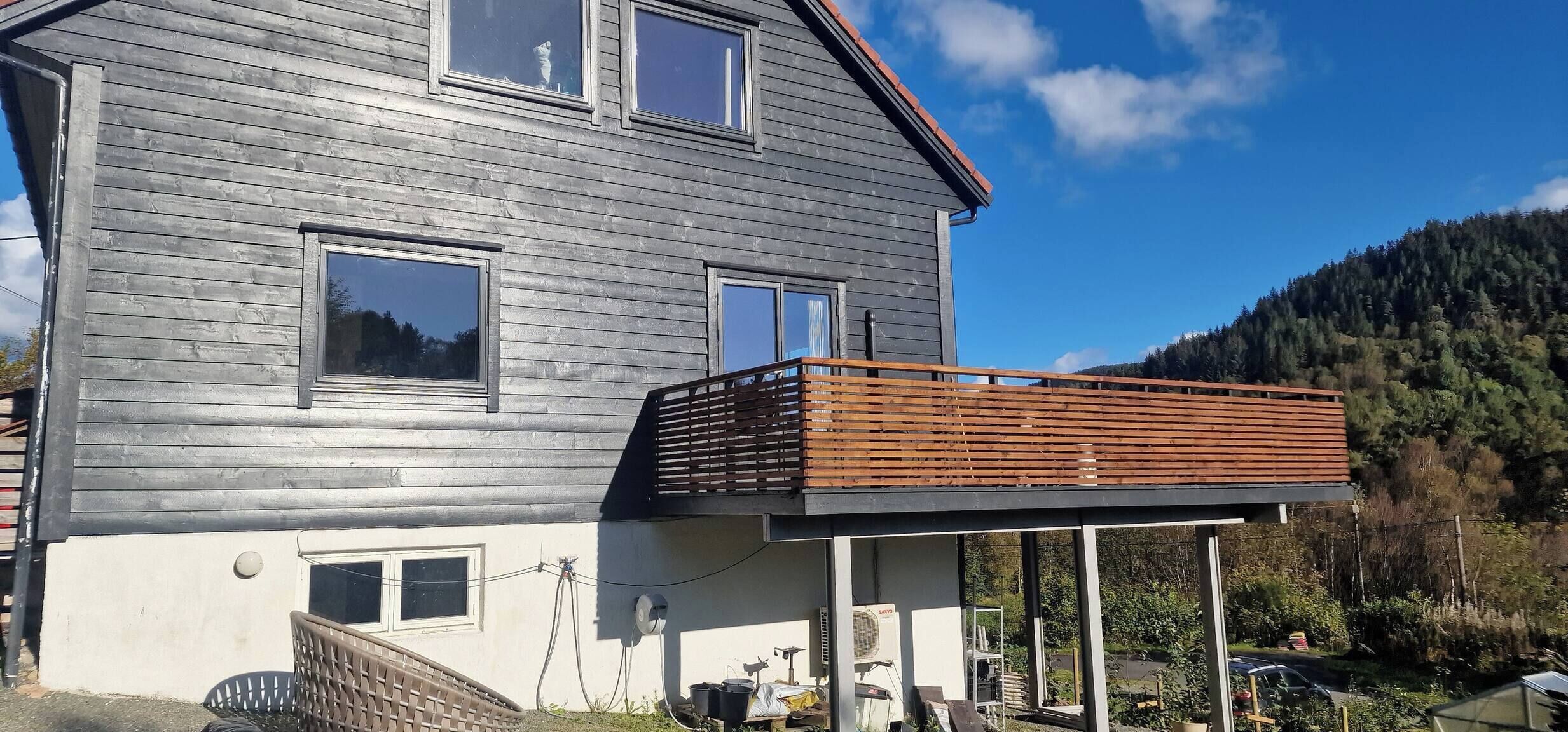 Een twee verdiepingen tellend huis met een balkon, een kleine aangebouwde garage, en een berg op de achtergrond.