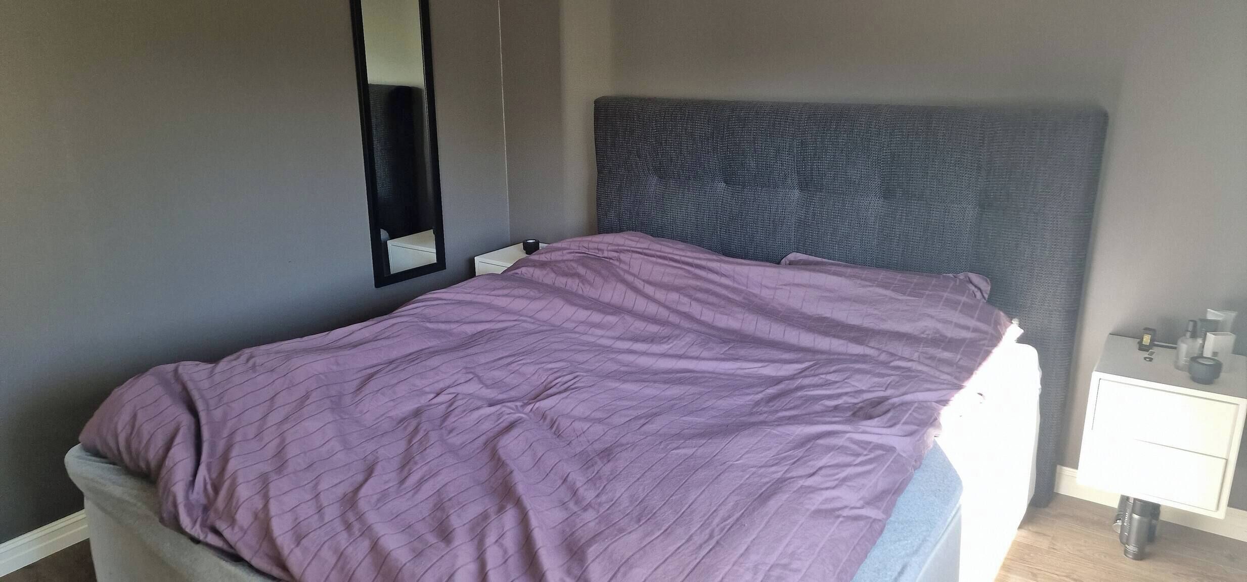 Un dormitorio con cama, mesita de noche, espejo y estante en la pared.