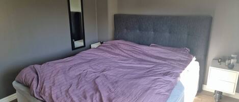 Un dormitorio con cama, mesita de noche, espejo y estante en la pared.