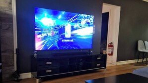 A modern living room with a large flat-screen TV, wooden flooring, a dark wall, and a fire extinguisher. - Charming House, 8 Beds, Possibility to Rent a Boat (Bjørnafjorden)