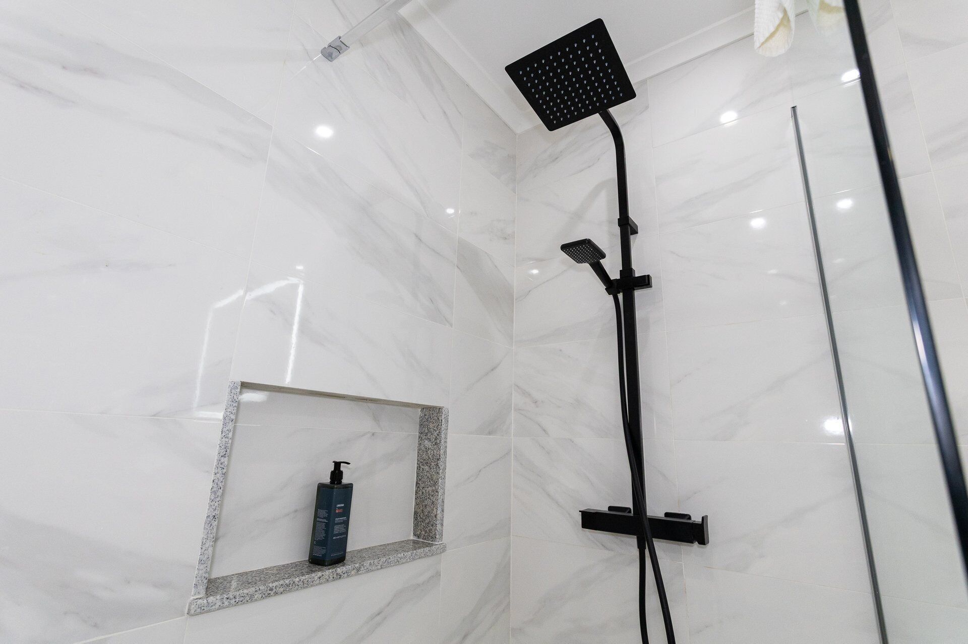 A modern bathroom with a shower, a mirror, and a bottle of shampoo.