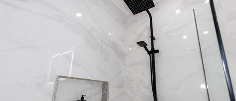 A modern bathroom with a shower, a mirror, and a bottle of shampoo.