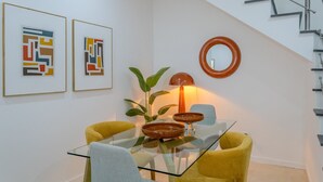 A dining area with a glass table, two yellow chairs, a plant, a lamp, and two abstract paintings on the wall.