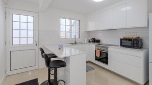 A modern kitchen with white cabinets, a central island, a microwave, a coffee maker, and a window.