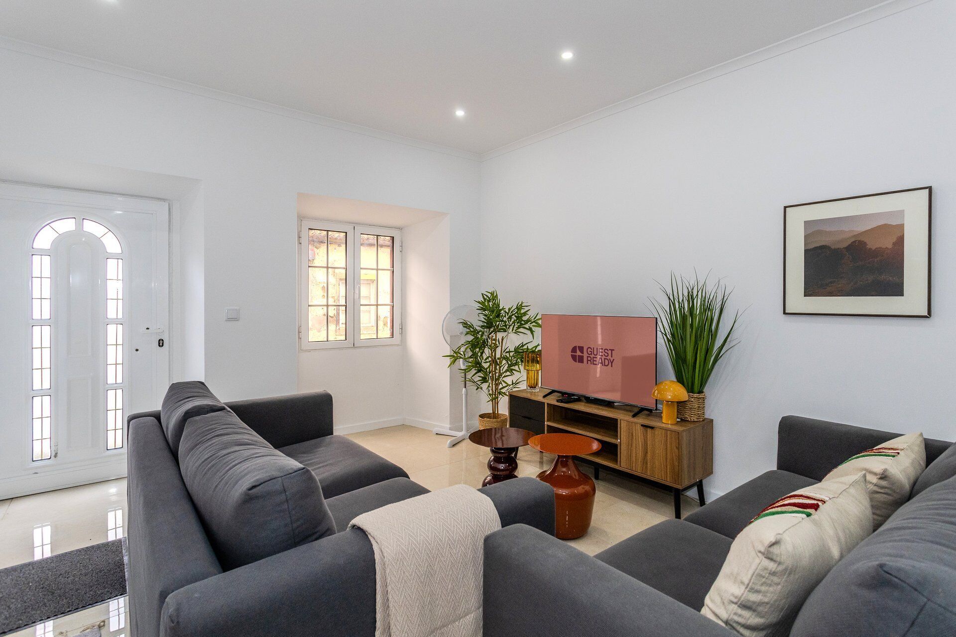 A modern living room with a sofa set, a flat-screen TV, a wooden side table, and a potted plant.