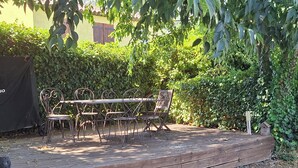 Eine Holzterrasse mit Tisch und Stühlen, umgeben von dichtem Grün und einer Mauer.