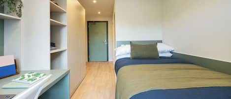 Een slaapkamer met een bed, een bureau en een deur naar een andere kamer.