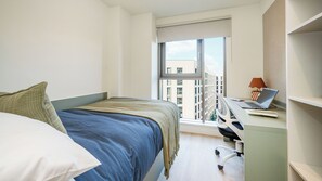 A bedroom with a bed, a desk with a laptop, and a window with a view of buildings. - For Students Only - City Wharf in Glasgow (Glasgow)