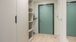 Um corredor com porta verde, prateleiras brancas e uma pequena planta.