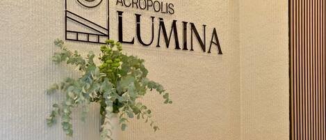 Una pared con el texto 'ACROPOLIS LUMINA' y una planta en maceta.