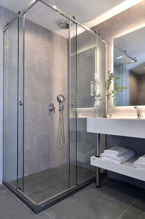 A modern bathroom with a glass-enclosed shower, a white vanity with a mirror, and a plant. - Acropolis Lumina (Athens)