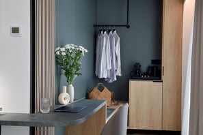 A modern kitchenette with a coffee machine, a hanging clothes rack, and a vase with flowers on a counter. - Acropolis Lumina (Athens)