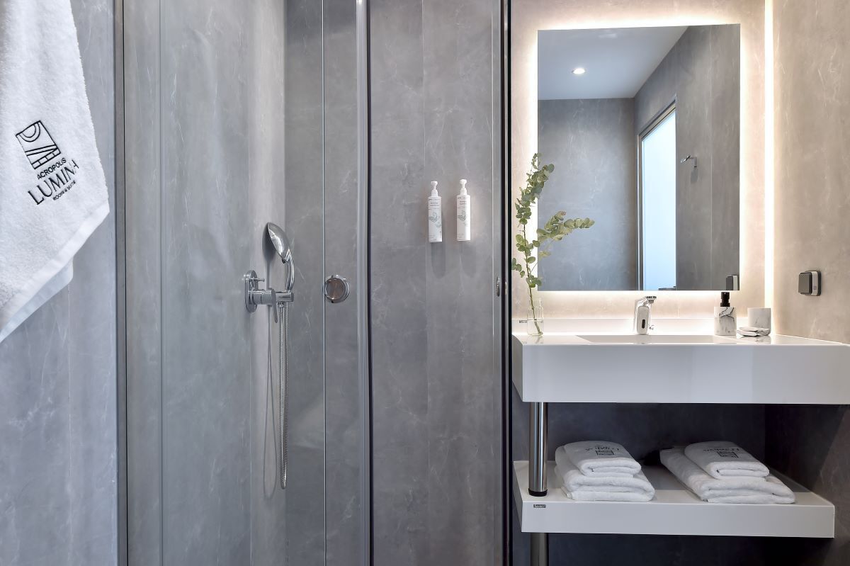 A modern bathroom with a glass shower enclosure, a white sink with a mirror above it, and neatly folded towels on a shelf.